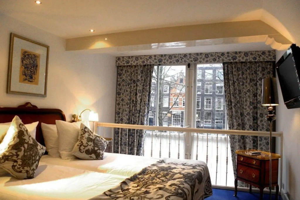 Elegant guest room with classic furnishings and views of historic canal houses at Ambassade Hotel Amsterdam.