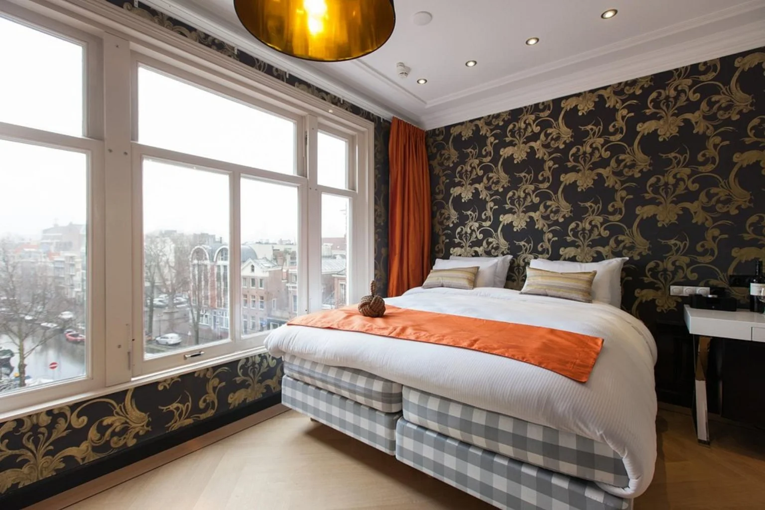 Elegant guest room with a comfortable bed, ornate decor and large windows overlooking the canal at Amsterdam Canal Hotel.