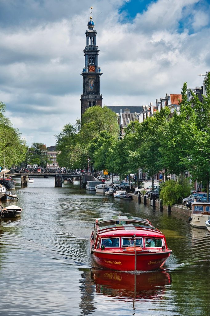 Amsterdam canal with a red tour boat and historic church tower