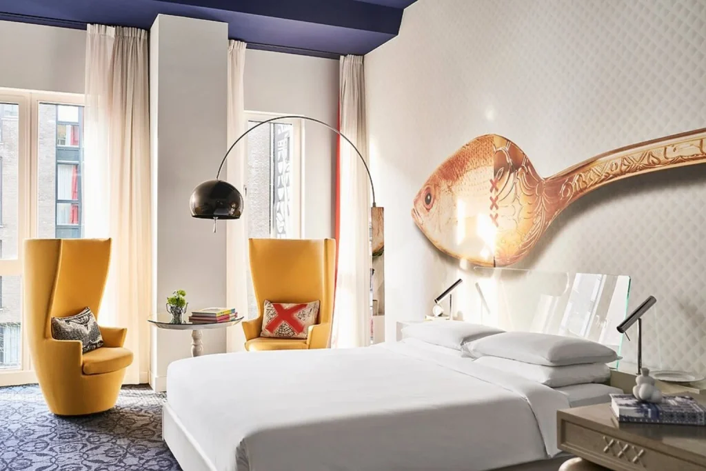 Creative designer bedroom featuring oversized fish wall art, vibrant yellow lounge chairs and contemporary furnishings at Andaz Amsterdam Prinsengracht, Amsterdam.