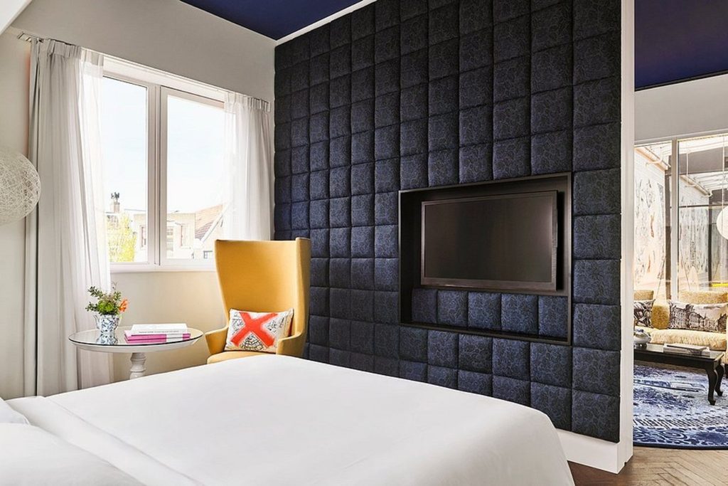 Stylish bedroom at Andaz Amsterdam Prinsengracht featuring a distinctive padded feature wall, contemporary furnishings and a bright adjoining living area.