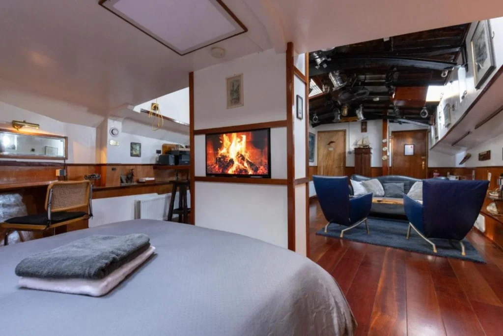 Cozy bedroom and living area with polished wooden floors, comfortable seating and a fireplace at Anna Houseboat Amsterdam.