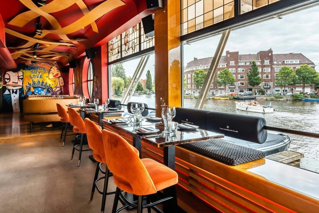 Stylish waterfront restaurant with colorful seating, contemporary decor and panoramic canal views at Apollo Hotel Amsterdam.