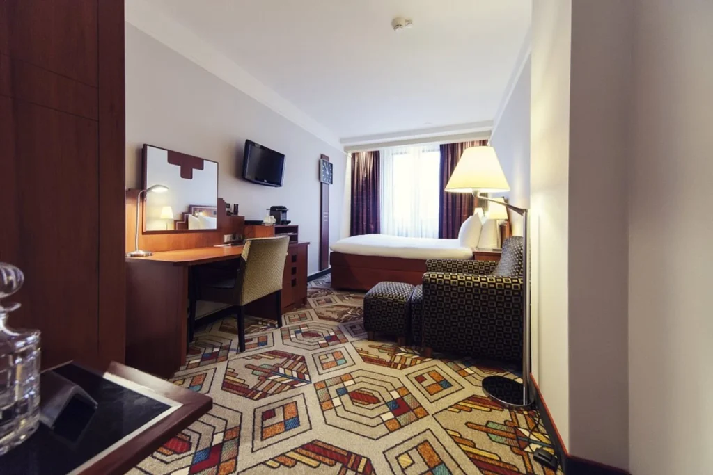 Comfortable guest room at Banks Mansion Amsterdam featuring a double bed, dedicated workspace, lounge chair and distinctive patterned carpet.