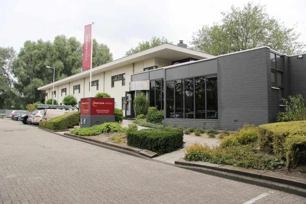 Low-rise hotel building surrounded by greenery with a parking area and entrance at the front, Bastion Hotel Amsterdam Noord, Amsterdam.
