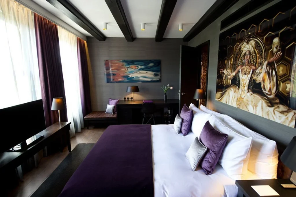 Luxury bedroom with purple accents, dark ceiling beams and artistic wall décor at Canal House Amsterdam