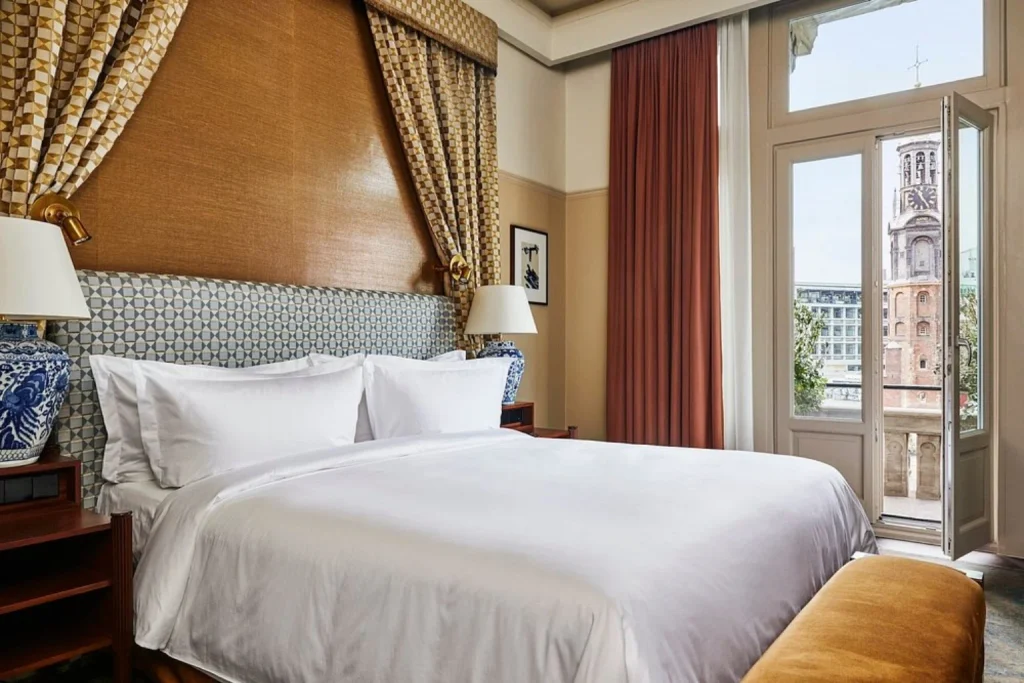 Luxury bedroom with open balcony and with patterned headboard and church tower view at De L’Europe Amsterdam