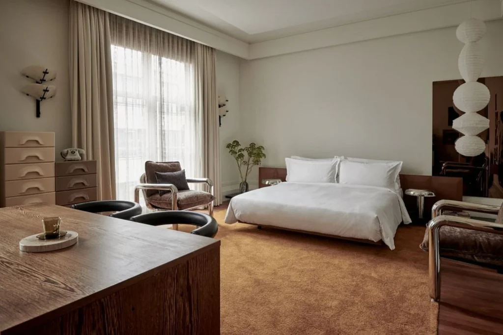 Sophisticated luxury bedroom featuring contemporary furnishings, designer seating, warm neutral tones and large windows at De L’Europe Amsterdam, Amsterdam.
