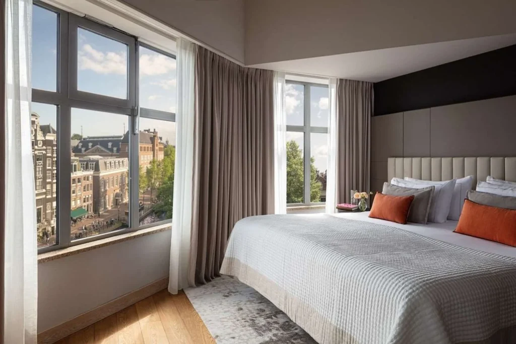 Grand deluxe room with large windows overlooking the city at Anantara Grand Hotel Krasnapolsky Amsterdam in Amsterdam, Netherlands