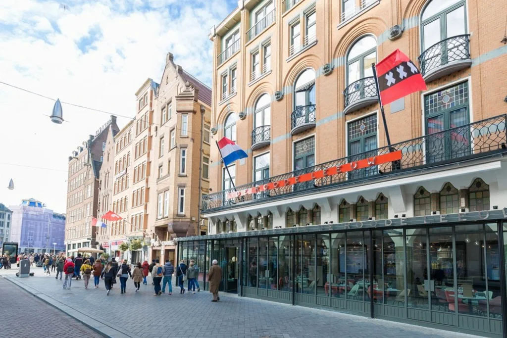 Historic facade with Dutch and Amsterdam flags along a busy city street at Hotel Amsterdam De Roode Leeuw.