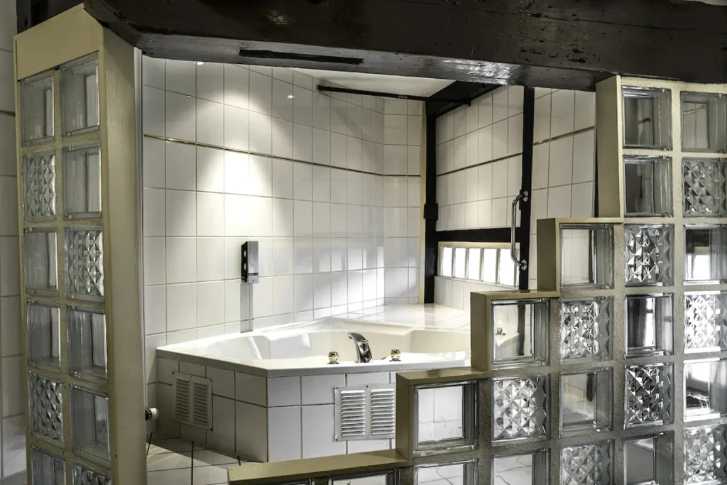 Private whirlpool bathtub surrounded by tiled walls and glass blocks at Hotel De Koopermoolen, Amsterdam.