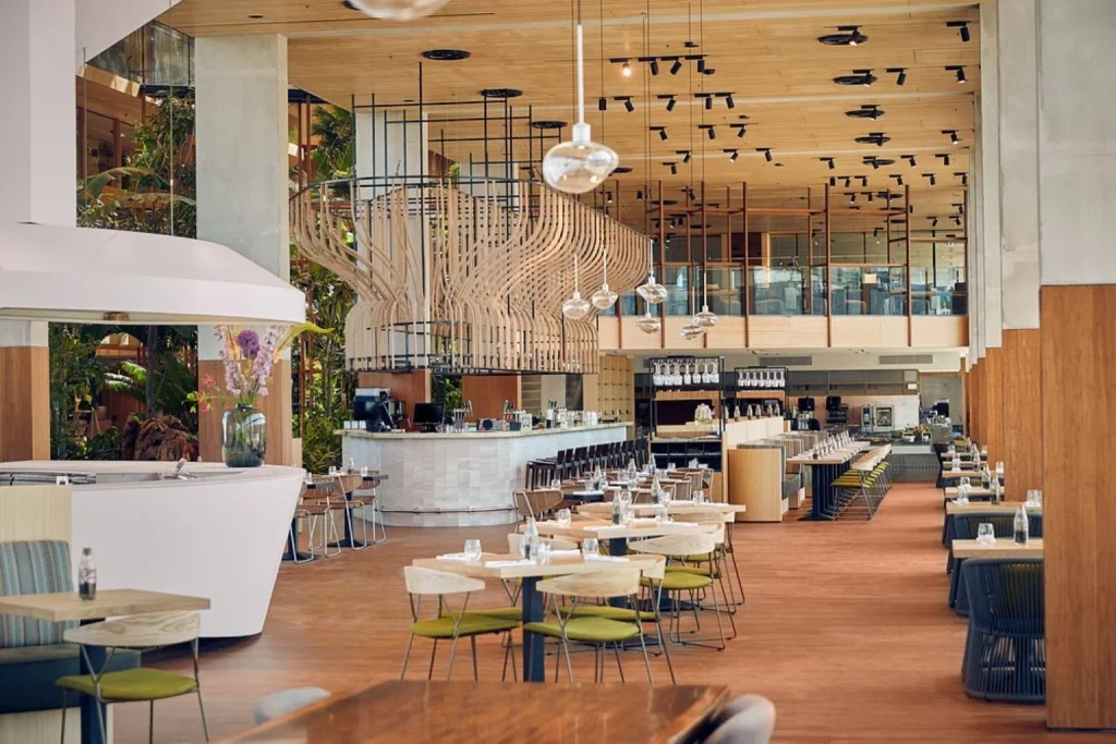 Spacious breakfast dining area with tropical greenery, contemporary interiors and an open kitchen at Hotel Jakarta Amsterdam.
