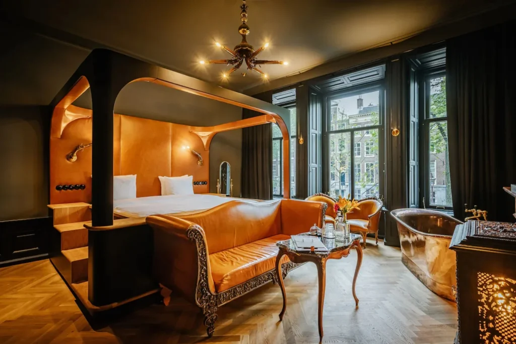 Elegant guest room featuring a four-poster bed, leather furnishings and freestanding bathtub at Hotel The Noblemen Amsterdam.