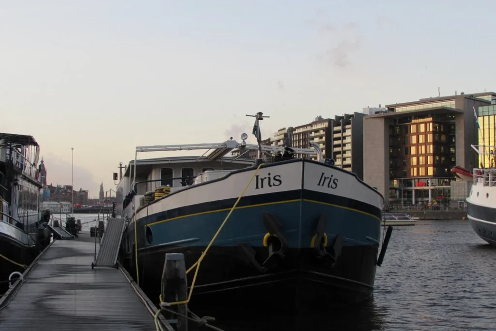 Moored houseboat overlooking the Amsterdam waterfront and surrounding city buildings at Hotelboat Iris Amsterdam.