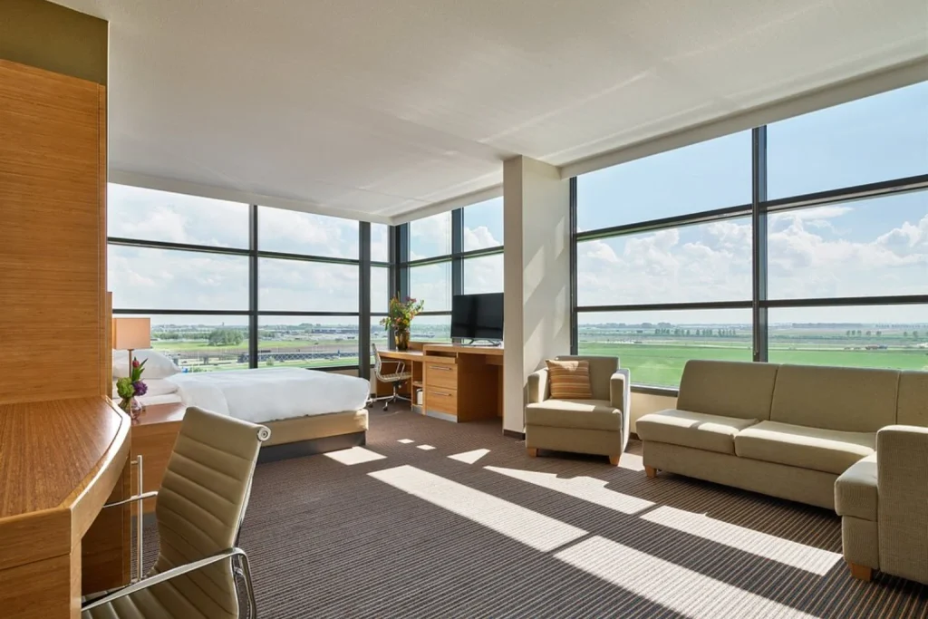 Bright and spacious room at Hyatt Place Amsterdam Airport with floor-to-ceiling windows, a seating area and panoramic views.