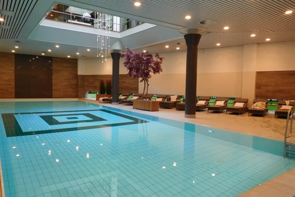 Large indoor swimming pool with poolside loungers and a modern wellness setting at Hotel Okura Amsterdam.