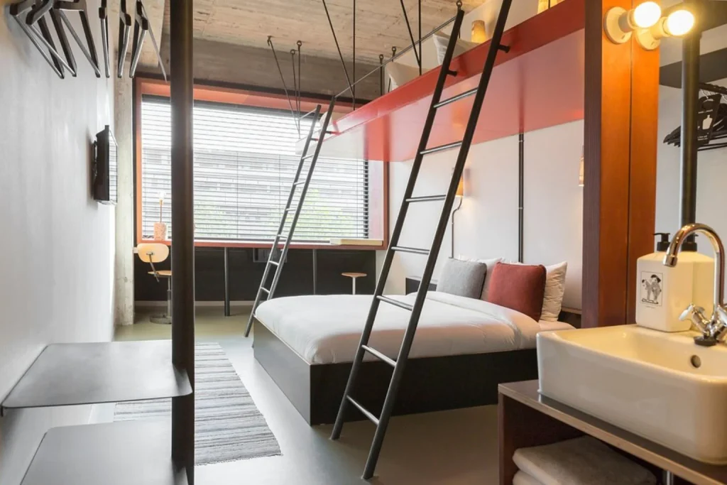 Industrial-style loft room with double bed, ladders and modern open design at Volkshotel, Amsterdam
