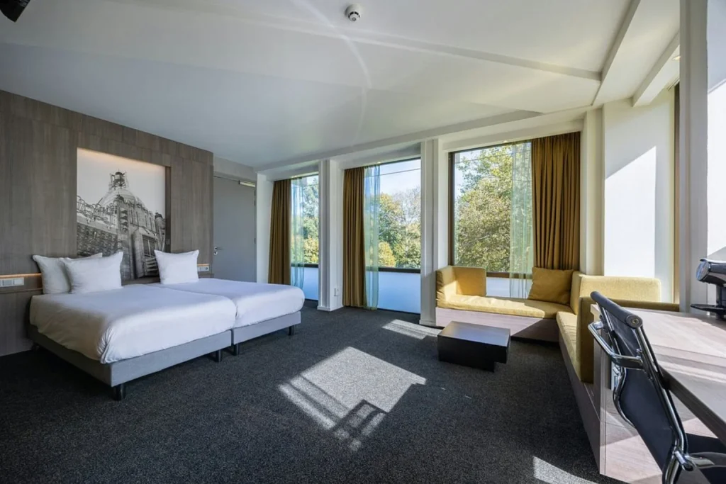 Bright contemporary guest room with twin beds, large windows and a comfortable seating area at Leonardo Hotel Amsterdam Rembrandtpark.