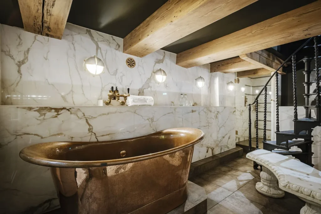 Luxury copper bathtub in a marble bathroom with wooden beams and spiral staircase at Hotel The Noblemen, Amsterdam