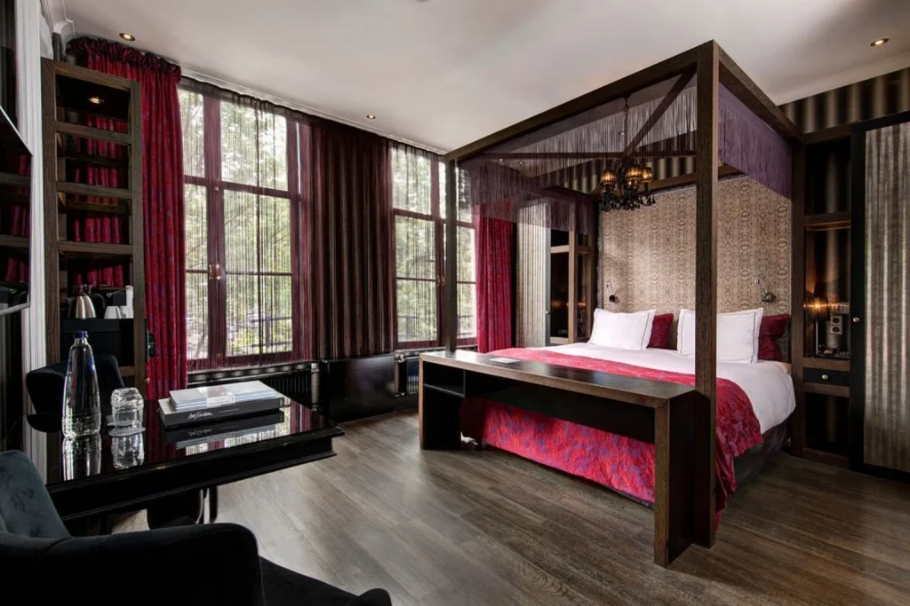 Luxury guest room with four-poster bed, dark romantic décor and large windows at The Toren, Amsterdam