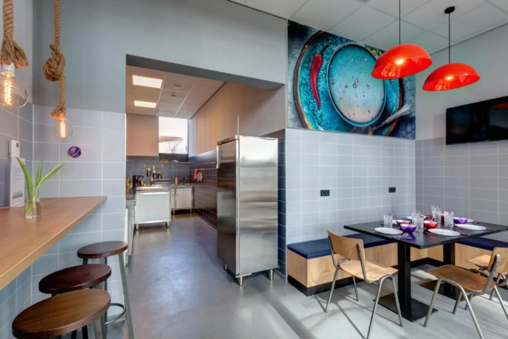 Colorful dining area with seating and access to the shared guest kitchen at MEININGER Hotel Amsterdam Amstel.
