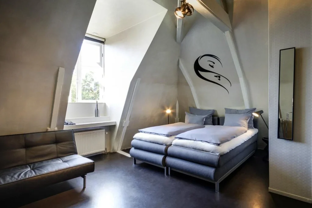 Modern attic hotel room with twin beds, exposed beams and large window at Hotel V Frederiksplein, Amsterdam