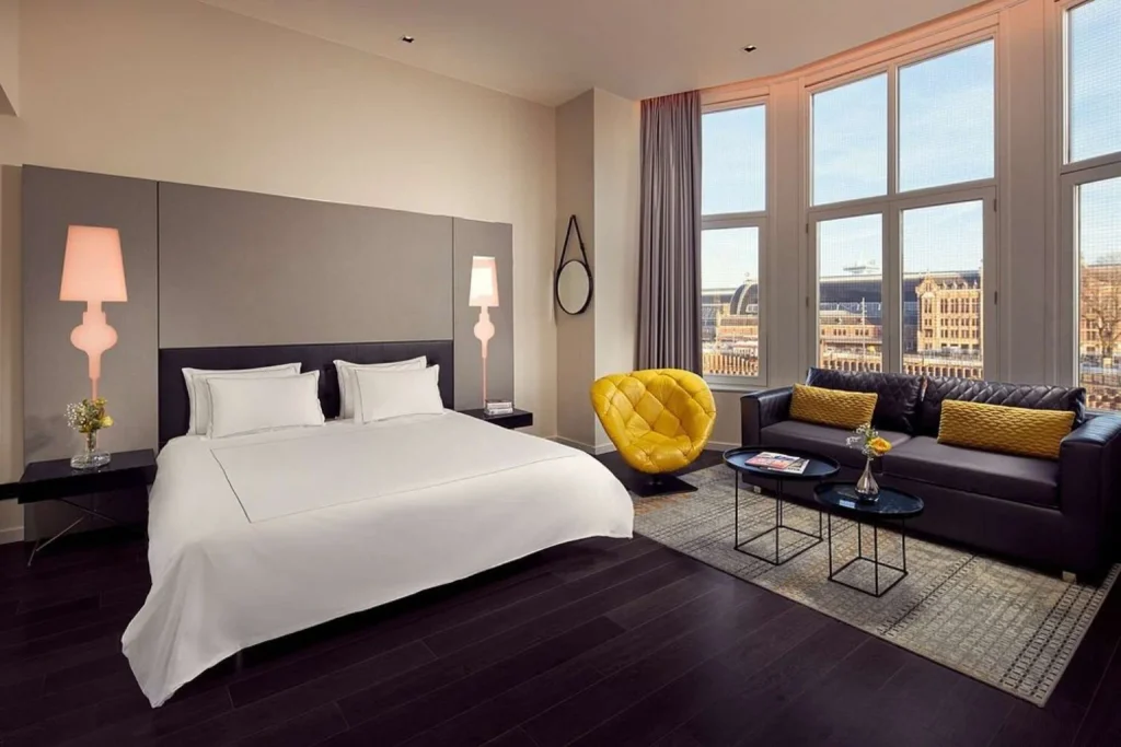 Spacious modern guest room with large windows, stylish seating area and city views at Park Plaza Victoria Amsterdam, Amsterdam.