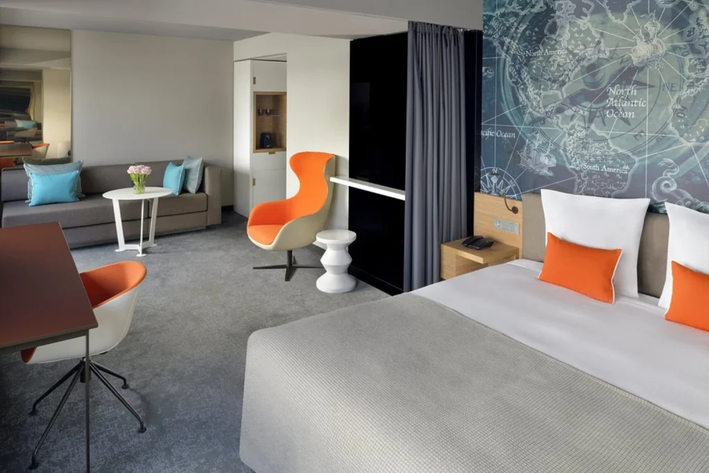 Spacious contemporary guest room with colorful seating, a lounge area and distinctive wall décor at Mövenpick Hotel Amsterdam City Centre.