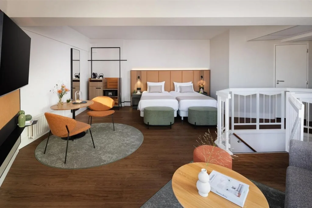 Spacious guest room with twin beds, modern furnishings and a comfortable seating area at NH City Centre Amsterdam.