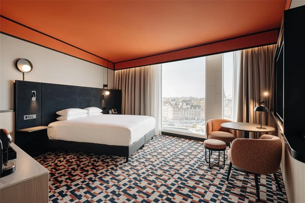 Contemporary guest room with dining area, comfortable seating and city views at NH Collection Amsterdam Barbizon Palace.