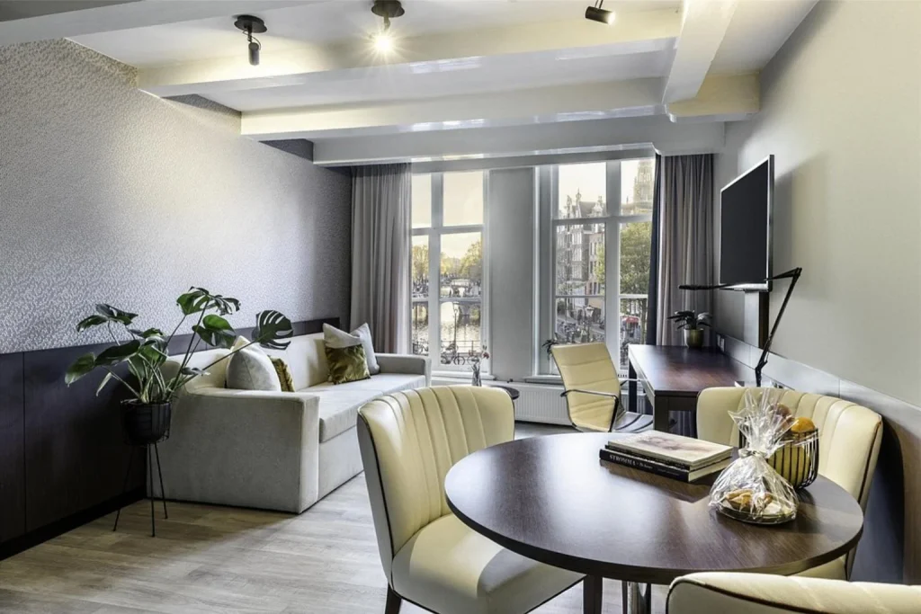 Contemporary guest room with a dining area, comfortable seating and views over Amsterdam at NH Collection Amsterdam Barbizon Palace.