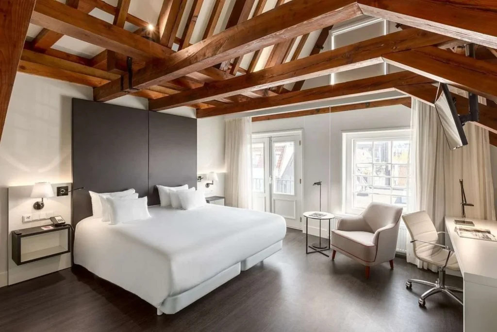 Bright hotel room with exposed wooden beams, a king-size bed, and seating area at NH Collection Barbizon Palace in Amsterdam