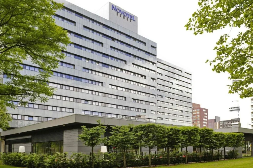 Modern hotel exterior surrounded by green trees and landscaped gardens at Novotel Amsterdam City, Amsterdam, Netherlands