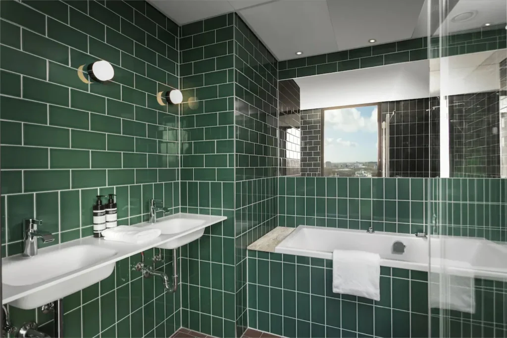 Modern bathroom with green tiles, double sinks, whirlpool bathtub and city views at Olympic Hotel Amsterdam.