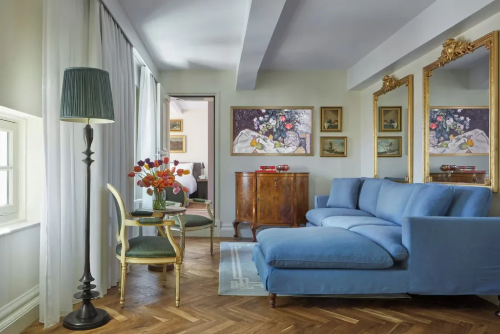 Elegant living area at Pulitzer Amsterdam featuring a blue sectional sofa, classic furnishings, artwork and large gilded mirrors.