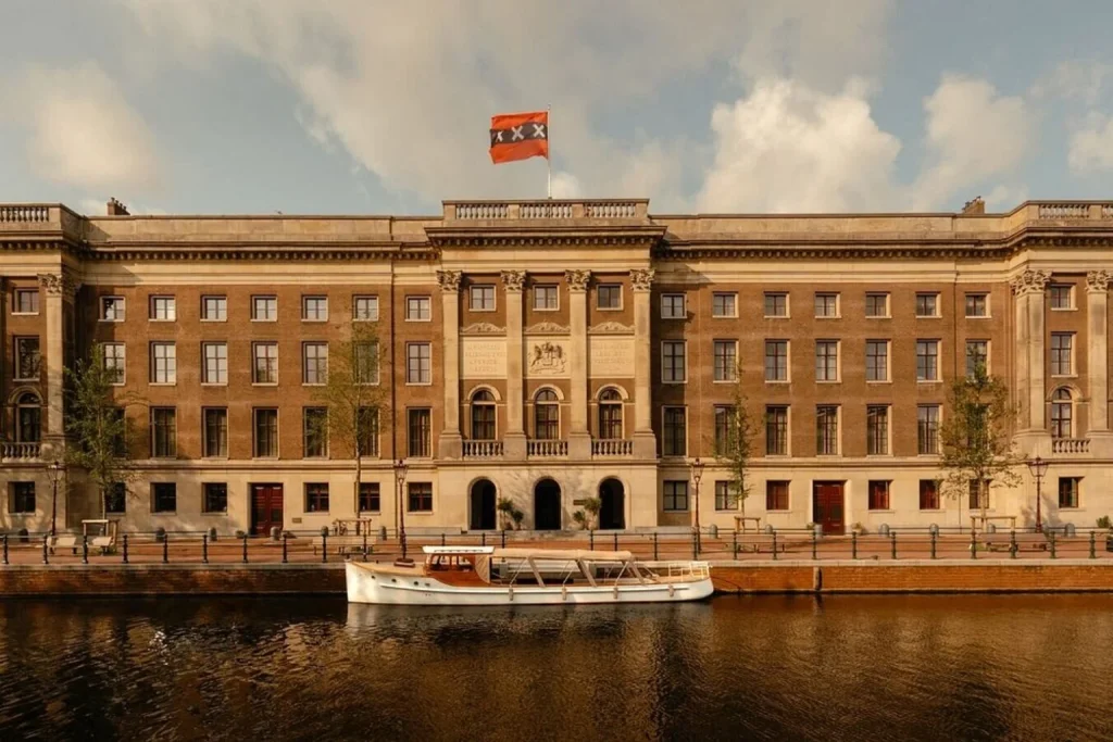 Grand historic waterfront building overlooking the canal with a classic boat moored in front, Rosewood Amsterdam, Amsterdam.