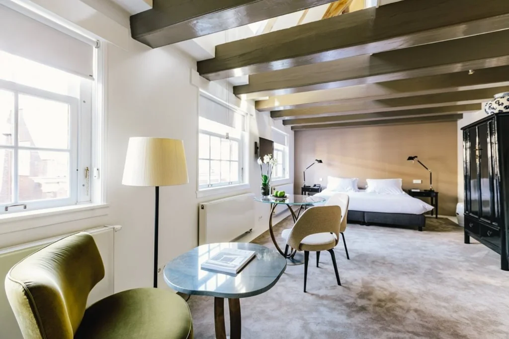 Spacious luxury guest room with exposed wooden beams, large windows and sitting area at The Dylan Amsterdam, Amsterdam