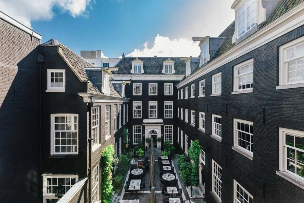 Elegant courtyard surrounded by historic black-brick architecture with outdoor dining tables and greenery, The Dylan Amsterdam, Amsterdam.