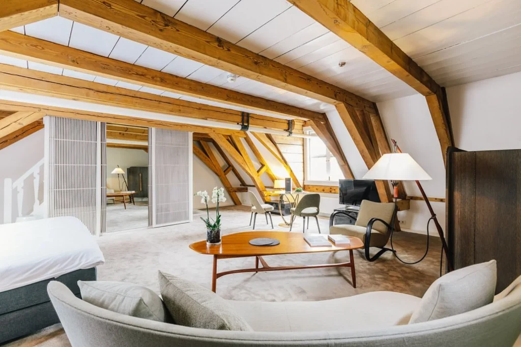 Spacious loft-style suite at The Dylan Amsterdam featuring exposed wooden beams, elegant lounge seating and a refined contemporary interior.
