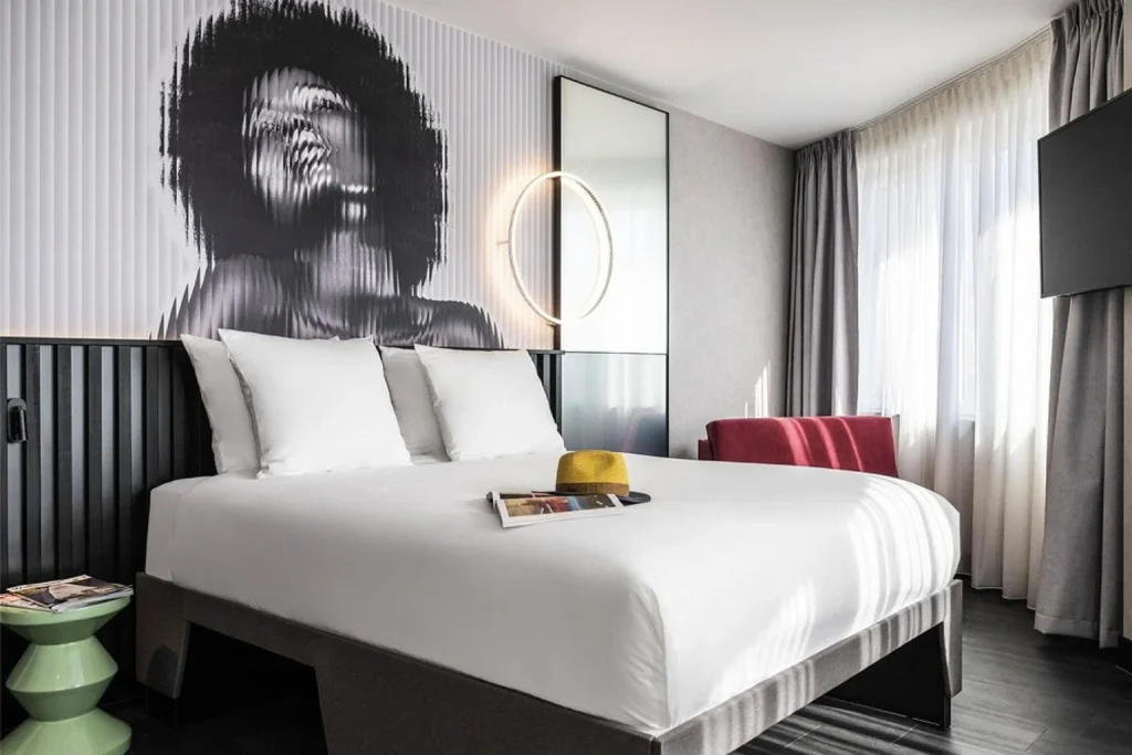 Modern hotel bedroom with double bed, artistic feature wall and large windows at Tribe Amsterdam City