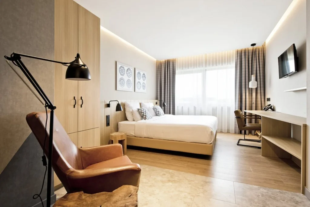 Spacious modern guest room with a double bed, dedicated workspace and leather lounge chair at Urban Lodge Hotel Amsterdam.