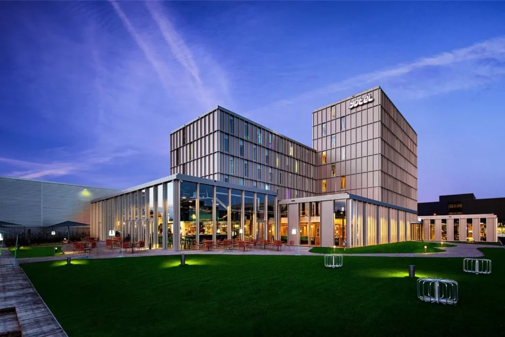 Contemporary hotel building illuminated at dusk with outdoor terraces and landscaped grounds at YOTEL Amsterdam, Amsterdam, Netherlands