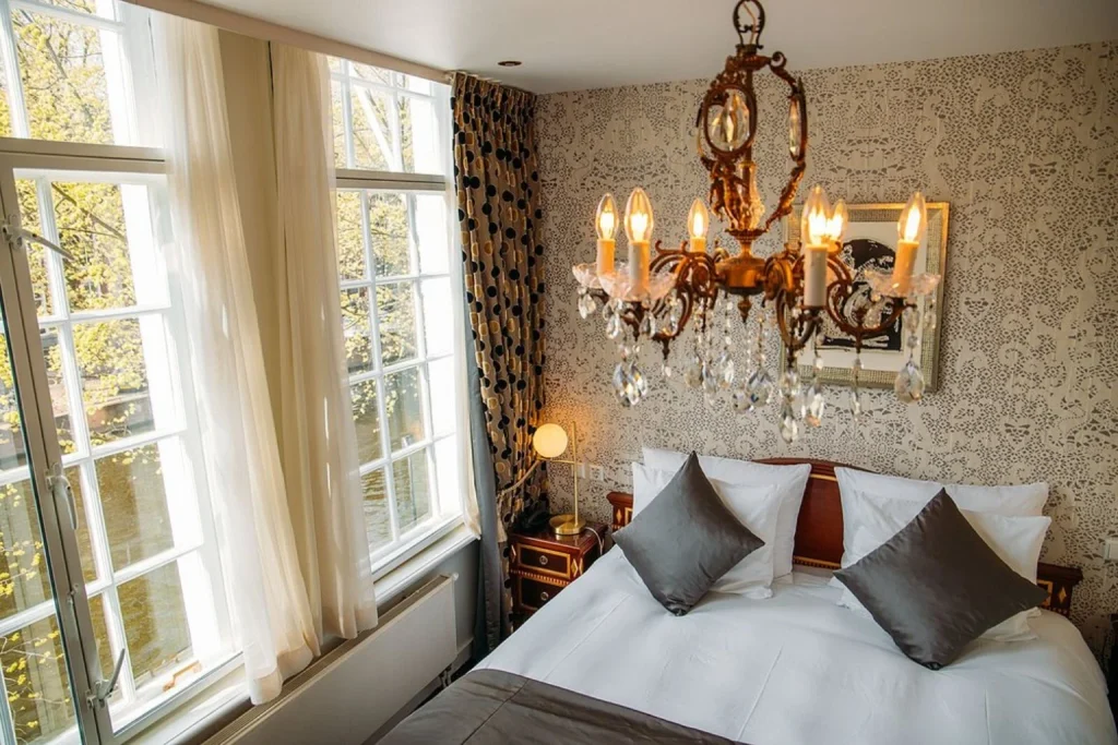 Elegant boutique hotel bedroom with crystal chandelier, double bed and large windows overlooking the canal at Ambassade Hotel in Amsterdam