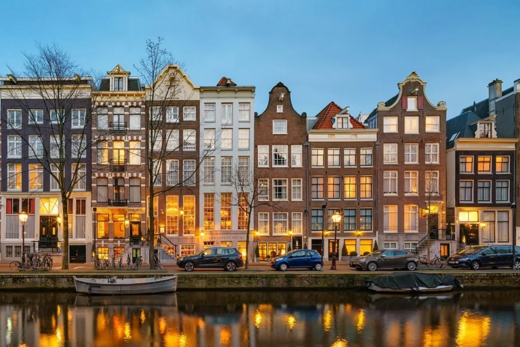 Historic canal houses forming the hotel exterior illuminated in the evening beside the water, Ambassade Hotel, Amsterdam