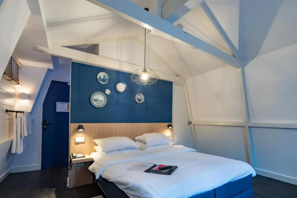 Bright guest room with a double bed, blue accent wall and distinctive exposed beams at Amistad Hotel, Amsterdam, Netherlands