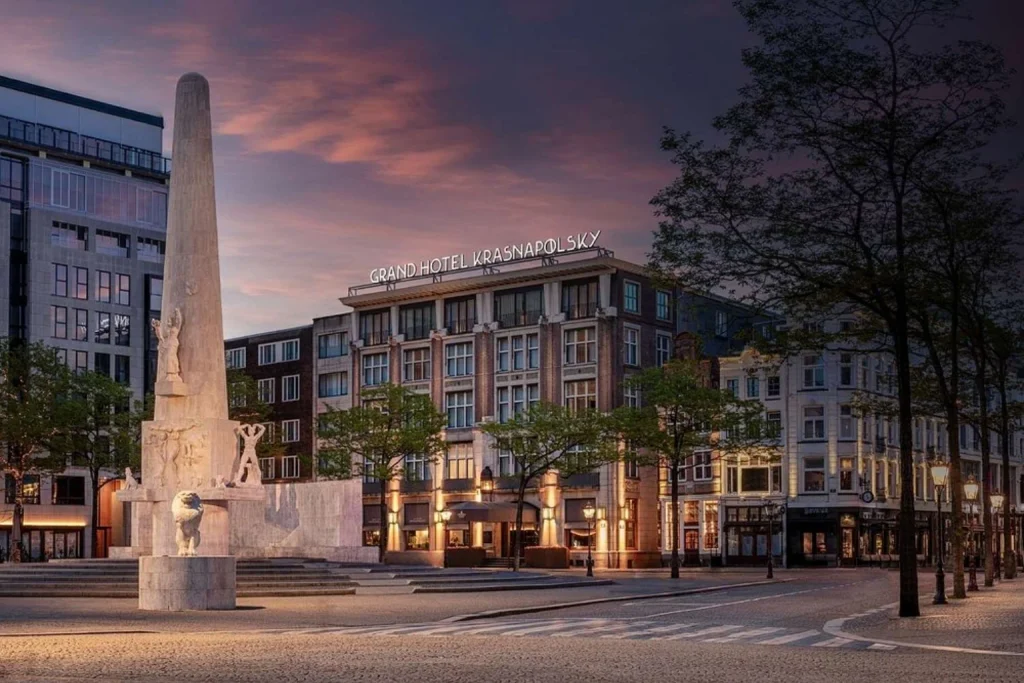 Grand hotel exterior illuminated at dusk beside the National Monument on Dam Square, Anantara Grand Hotel Krasnapolsky Amsterdam, Amsterdam
