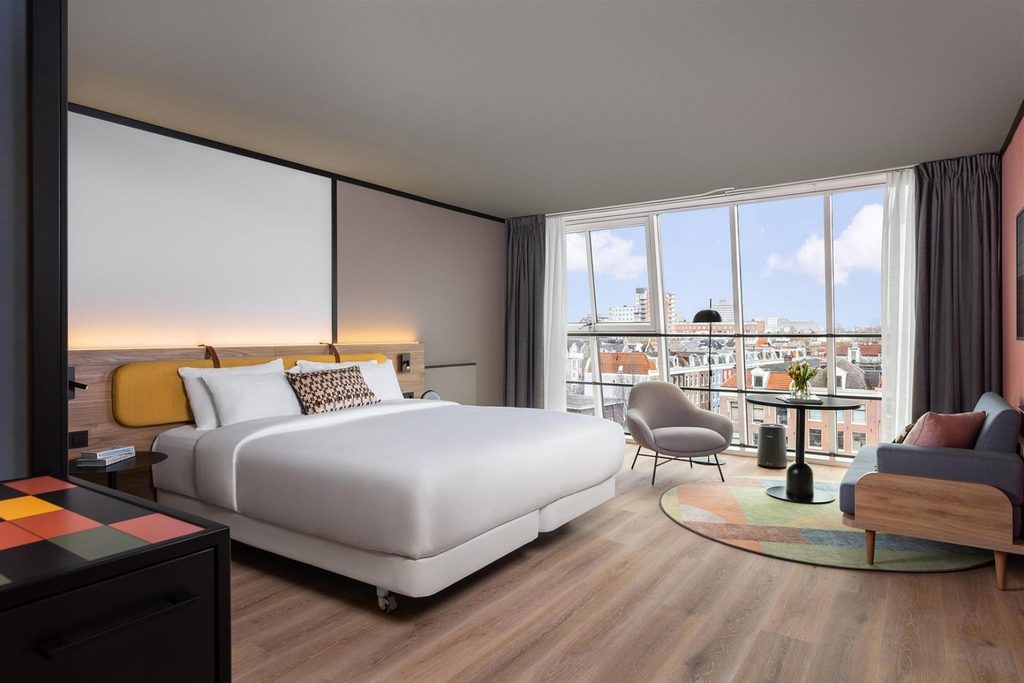 Spacious modern hotel room with king bed, lounge seating and floor-to-ceiling windows with city views at Avani Museum Quarter, Amsterdam