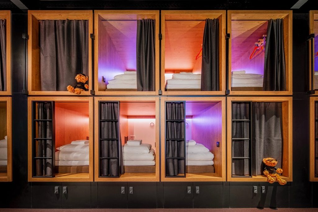 Stacked wooden sleeping pods with privacy curtains and colorful lighting at BUNK Hotel Amsterdam, Amsterdam, Netherlands