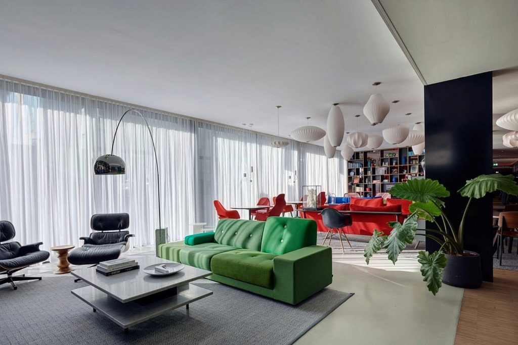 Stylish hotel lounge with green sofa, designer chairs, red seating and floor-to-ceiling windows at citizenM Amsterdam South in Amsterdam
