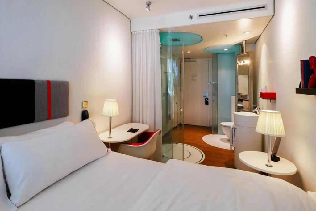 Compact modern guest room with a large bed, glass shower and contemporary interior at citizenM Amsterdam South, Amsterdam